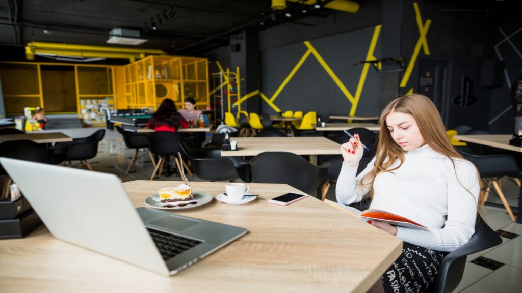 A woman working at a hot desk with a laptop, coffee, and notebook